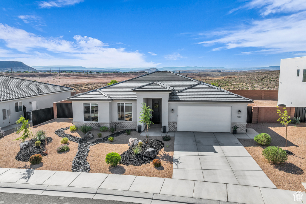 View of front of house with an attached garage, stucco siding, concrete driveway, a mountain view, and a tiled roof