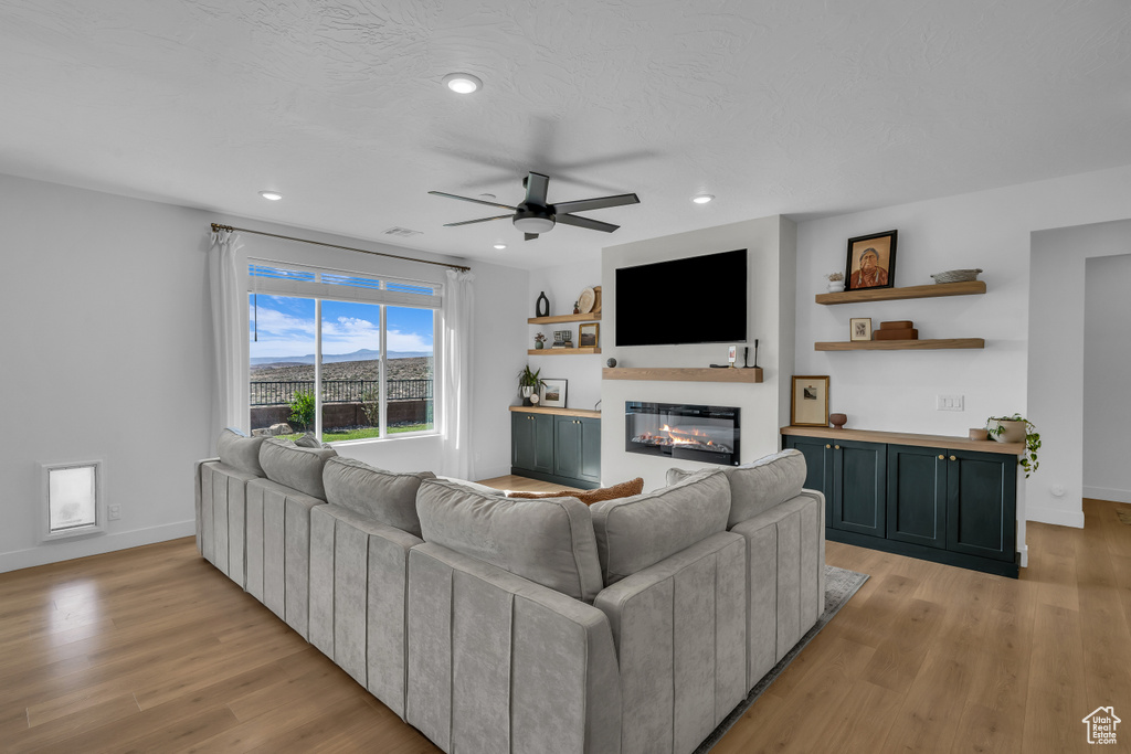Living area with a glass covered fireplace, light wood-style flooring, a ceiling fan, baseboards, and recessed lighting