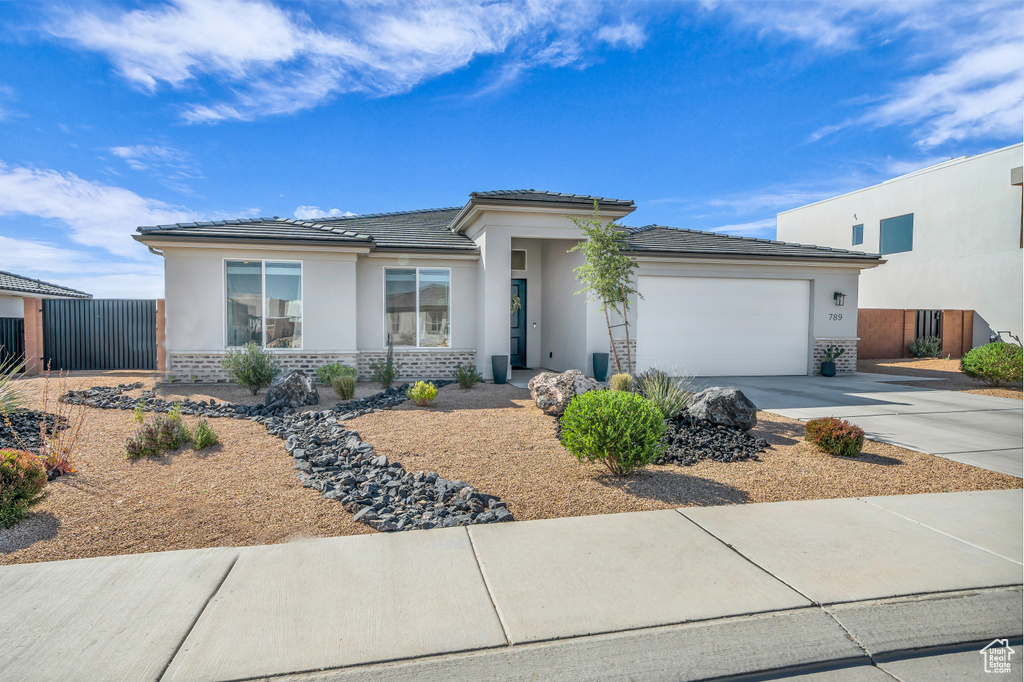 Prairie-style house with an attached garage, stucco siding, driveway, and brick siding