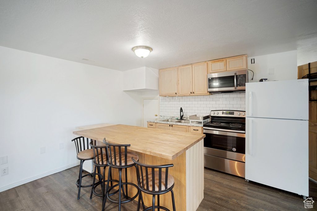Kitchen with a sink, light brown cabinetry, dark wood-style flooring, butcher block countertops, and appliances with stainless steel finishes