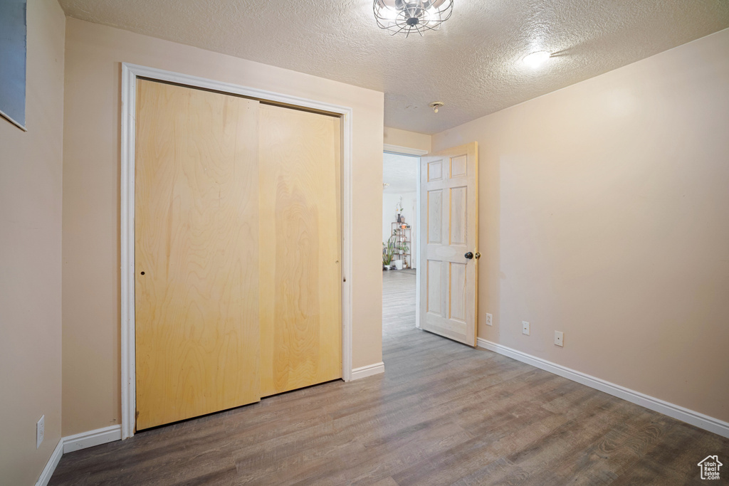 Unfurnished bedroom with a textured ceiling, a closet, baseboards, and wood finished floors
