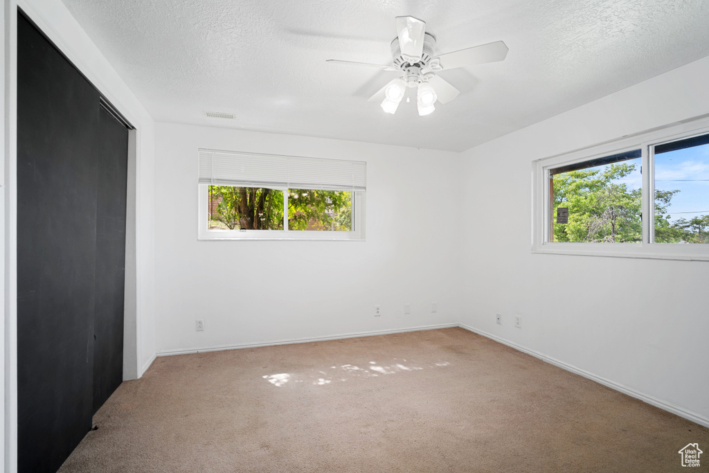 Unfurnished room featuring carpet, baseboards, ceiling fan, and plenty of natural light