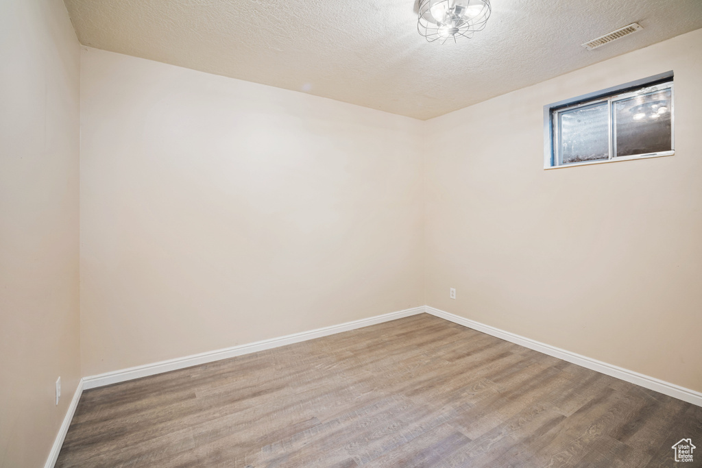 Spare room with baseboards, visible vents, a textured ceiling, and wood finished floors