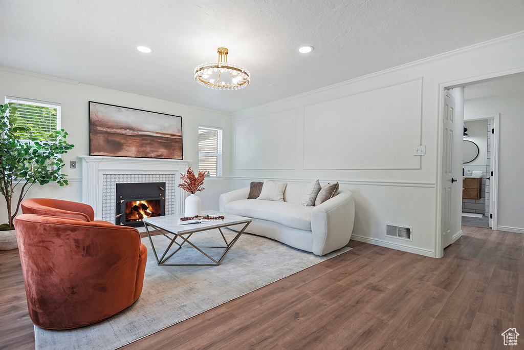 Living area featuring wood finished floors, plenty of natural light, a tile fireplace, crown molding, and a chandelier