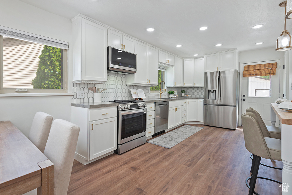 Kitchen with stainless steel appliances, a sink, wood finished floors, white cabinetry, and recessed lighting