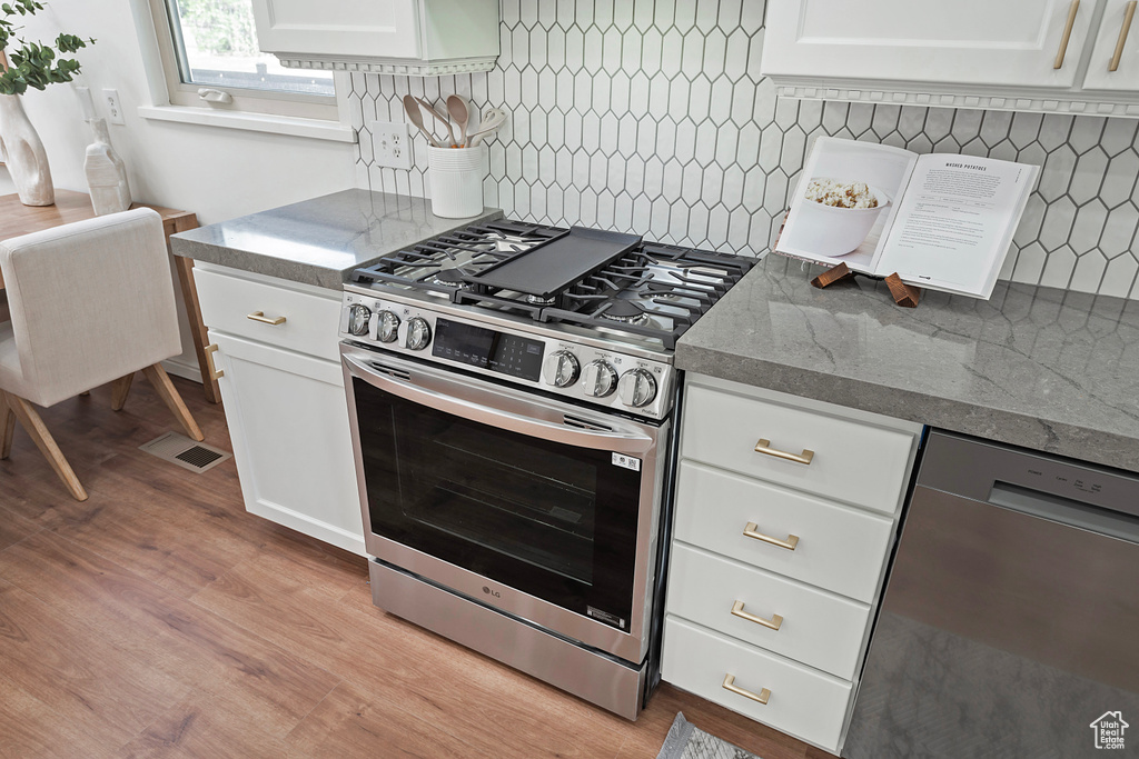 Kitchen featuring stainless steel appliances, backsplash, white cabinetry, and light wood-style flooring