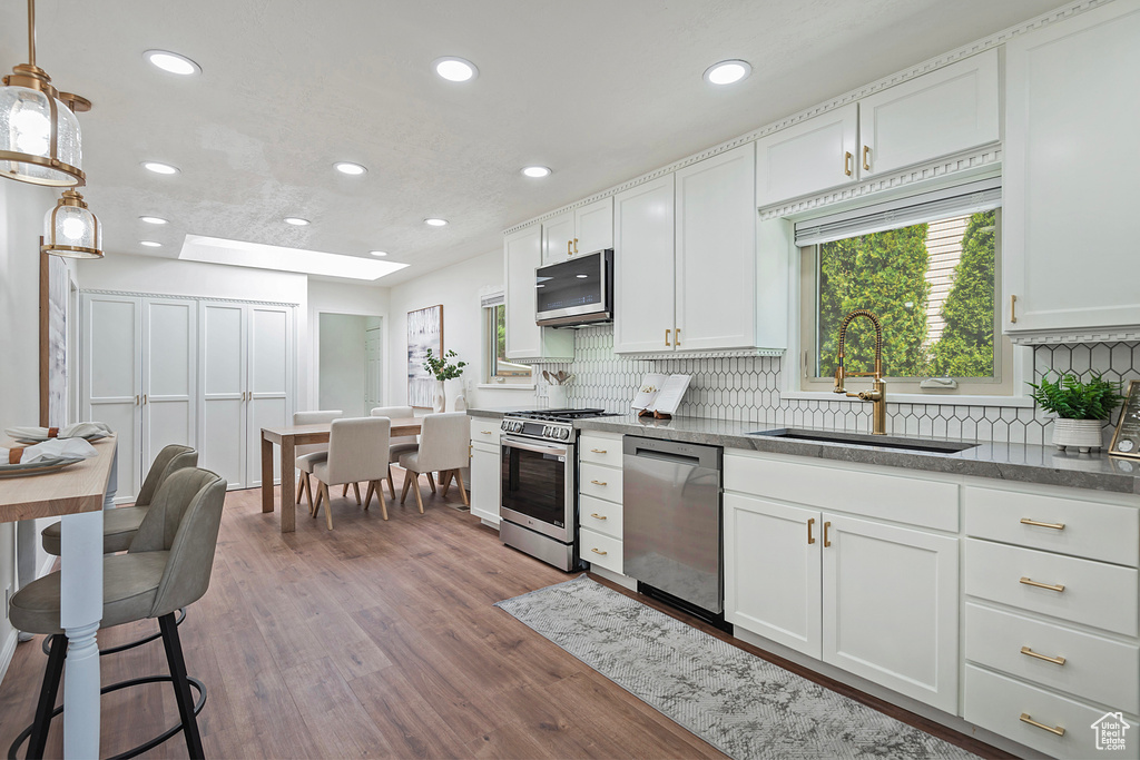 Kitchen with a sink, appliances with stainless steel finishes, backsplash, recessed lighting, and wood finished floors