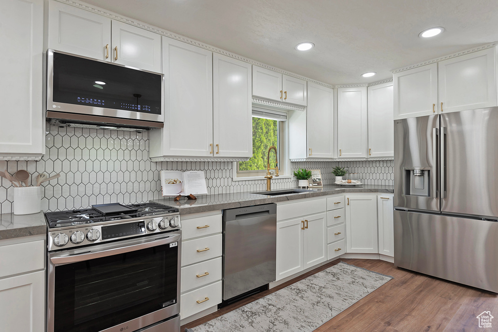 Kitchen featuring appliances with stainless steel finishes, a sink, white cabinets, decorative backsplash, and recessed lighting