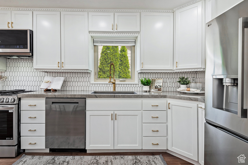 Kitchen with stainless steel appliances, a sink, white cabinetry, and decorative backsplash