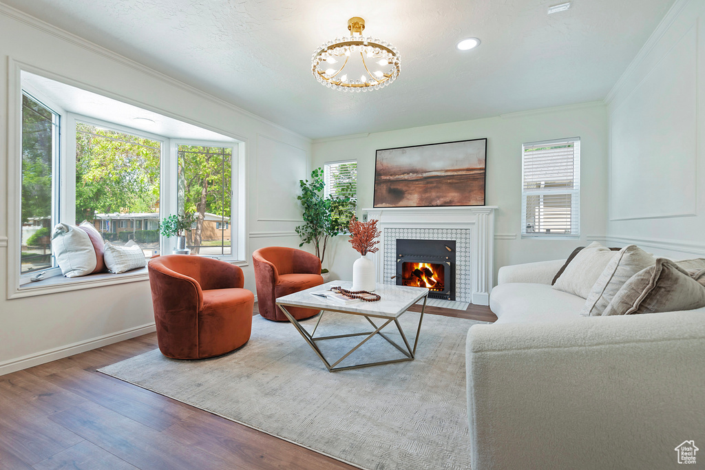 Living area featuring wood finished floors, a tiled fireplace, plenty of natural light, crown molding, and a chandelier