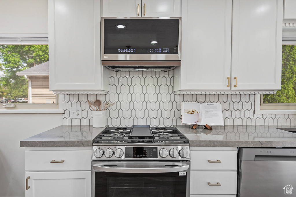 Kitchen featuring appliances with stainless steel finishes, white cabinetry, healthy amount of natural light, and decorative backsplash