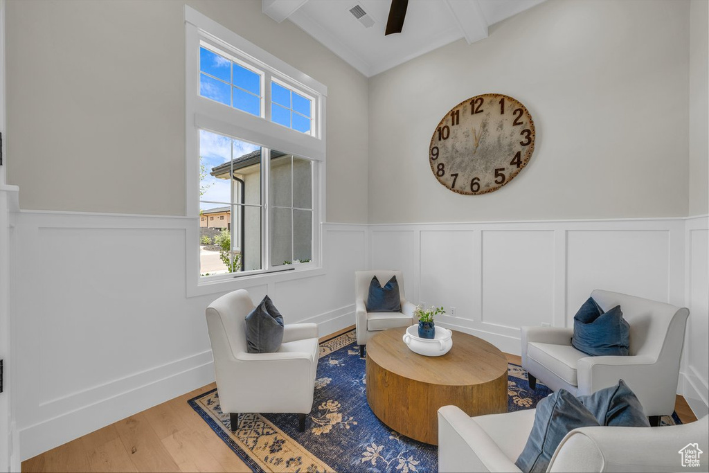 Sitting room with beamed ceiling, a decorative wall, a ceiling fan, wood finished floors, and wainscoting