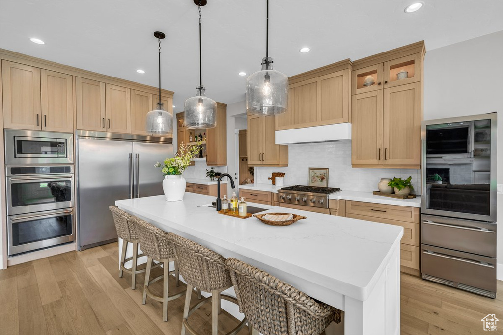 Kitchen featuring built in appliances, exhaust hood, a kitchen bar, tasteful backsplash, and a sink