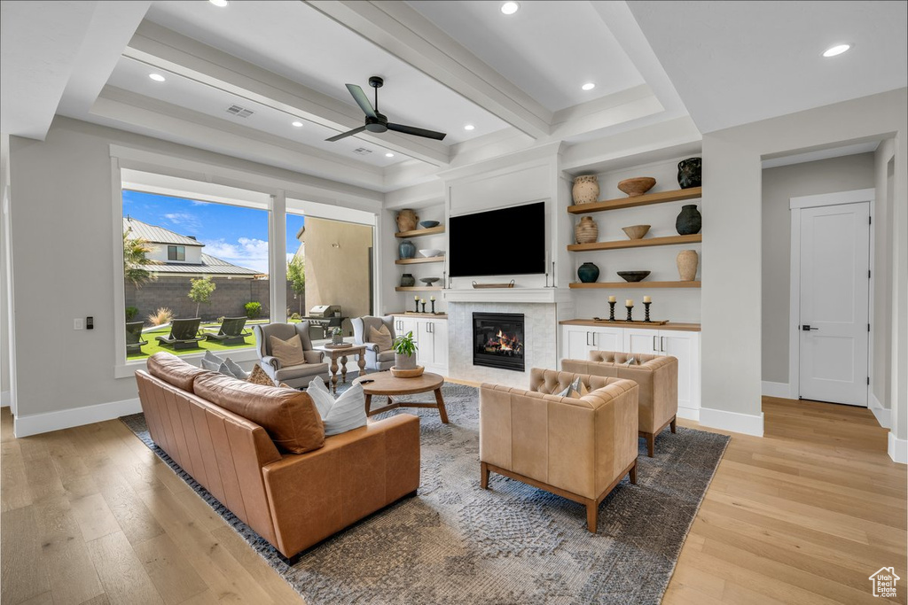 Living area featuring ceiling fan, light wood-style flooring, a glass covered fireplace, baseboards, and beamed ceiling