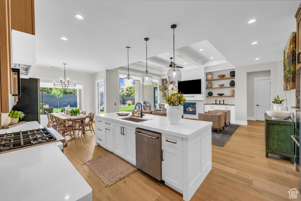 Kitchen featuring stainless steel dishwasher, a sink, a glass covered fireplace, light wood finished floors, and light countertops
