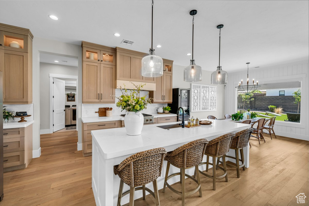 Kitchen with a sink, backsplash, light wood-style flooring, a kitchen breakfast bar, and recessed lighting