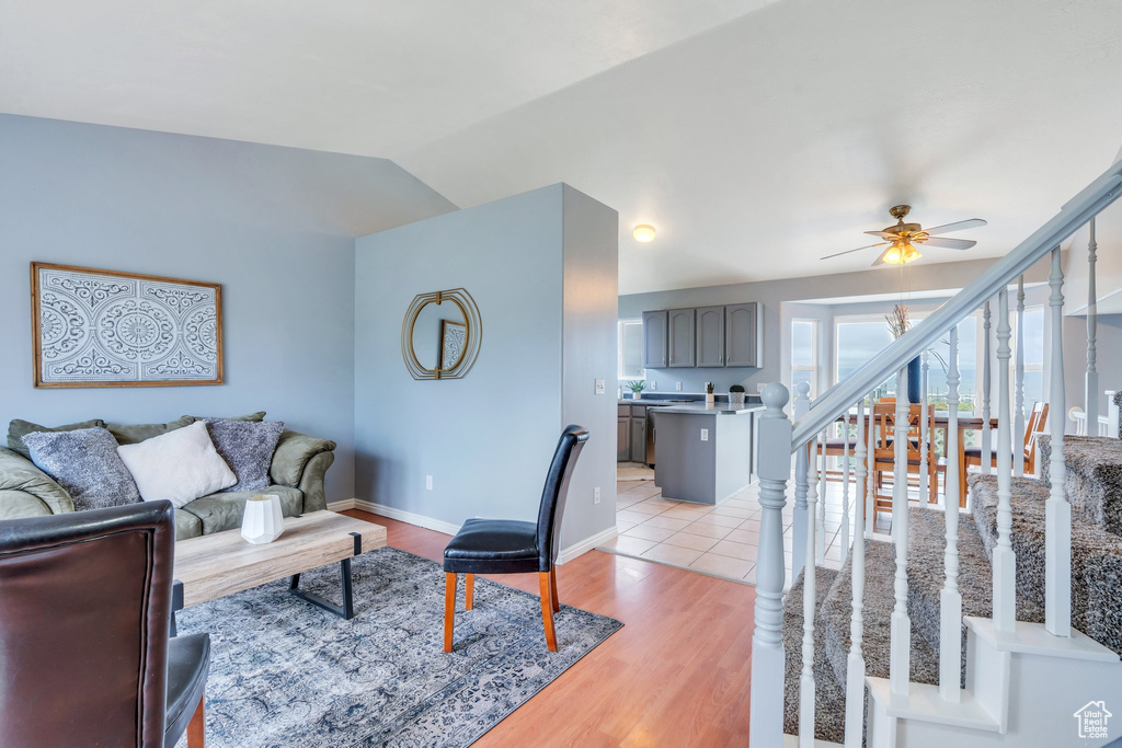 Living room with a ceiling fan, vaulted ceiling, light wood-style floors, stairway, and baseboards