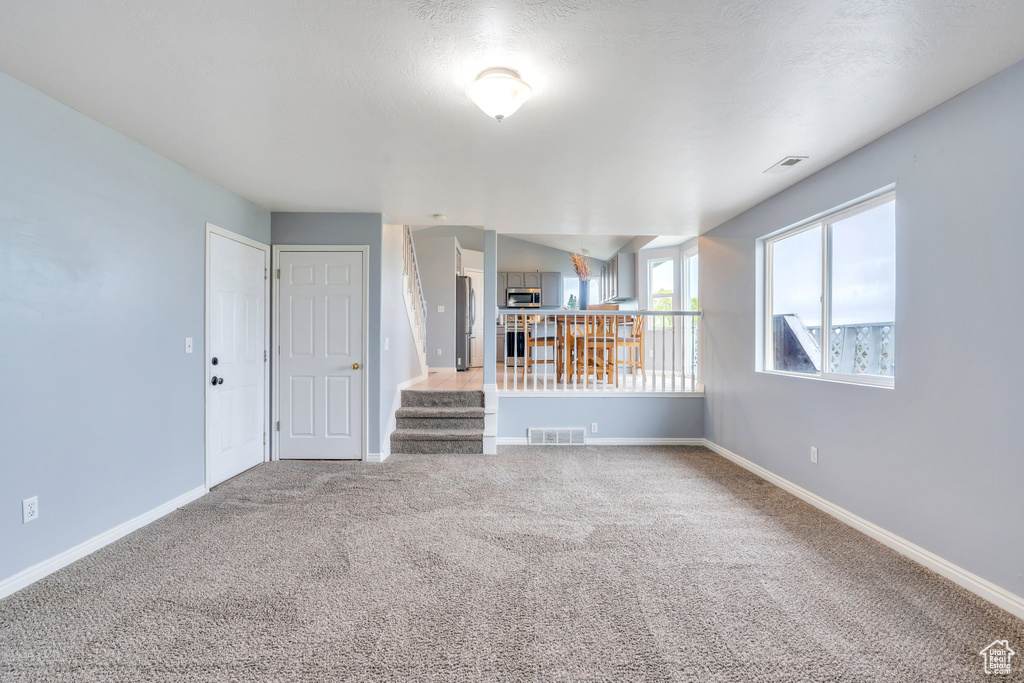 Unfurnished living room with carpet flooring, baseboards, and stairway