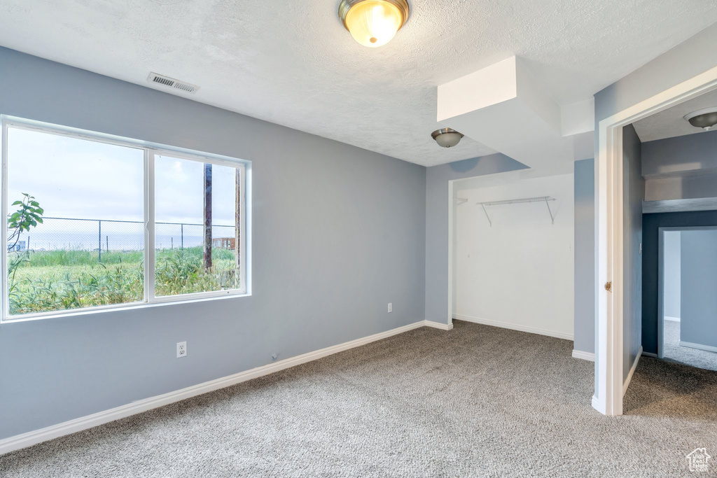 Unfurnished bedroom with carpet, multiple windows, a textured ceiling, baseboards, and a closet