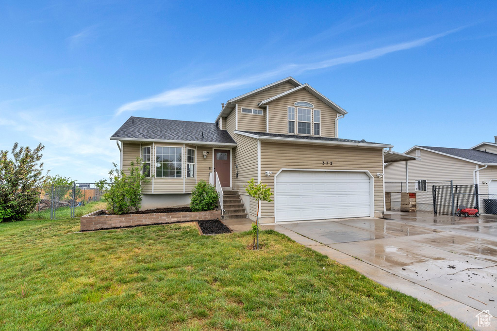 Tri-level home featuring an attached garage, concrete driveway, and a gate