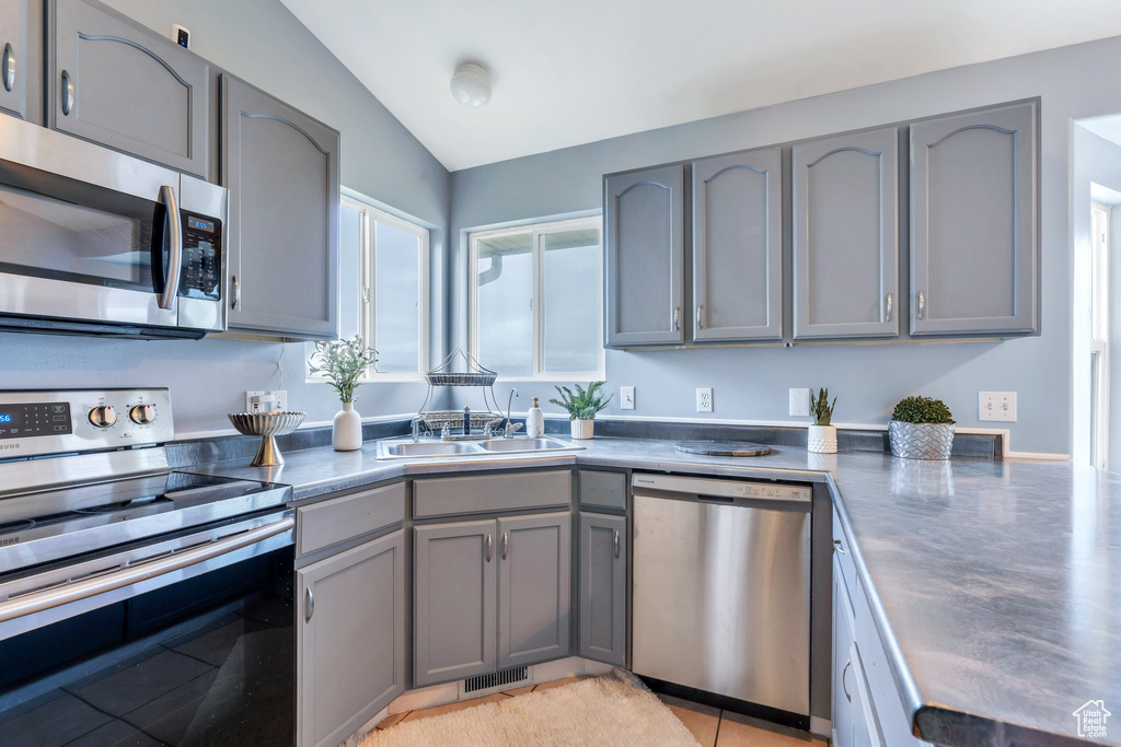 Kitchen with appliances with stainless steel finishes, gray cabinets, vaulted ceiling, a sink, and dark countertops