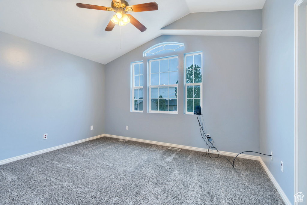 Carpeted empty room with lofted ceiling, ceiling fan, and baseboards