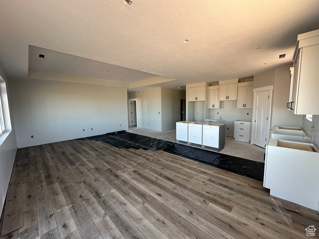 Kitchen featuring open floor plan, hardwood / wood-style flooring, a textured ceiling, white cabinets, and a center island