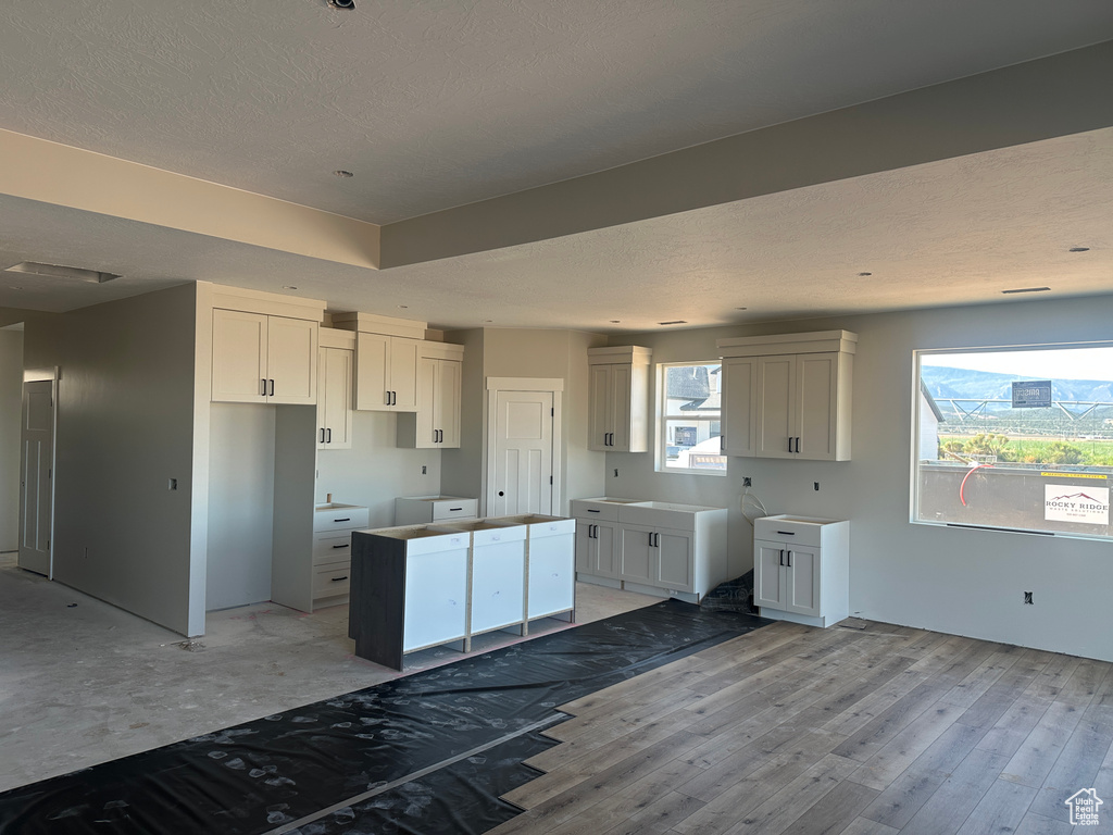 Kitchen with a center island, a textured ceiling, light wood-style flooring, and white cabinetry
