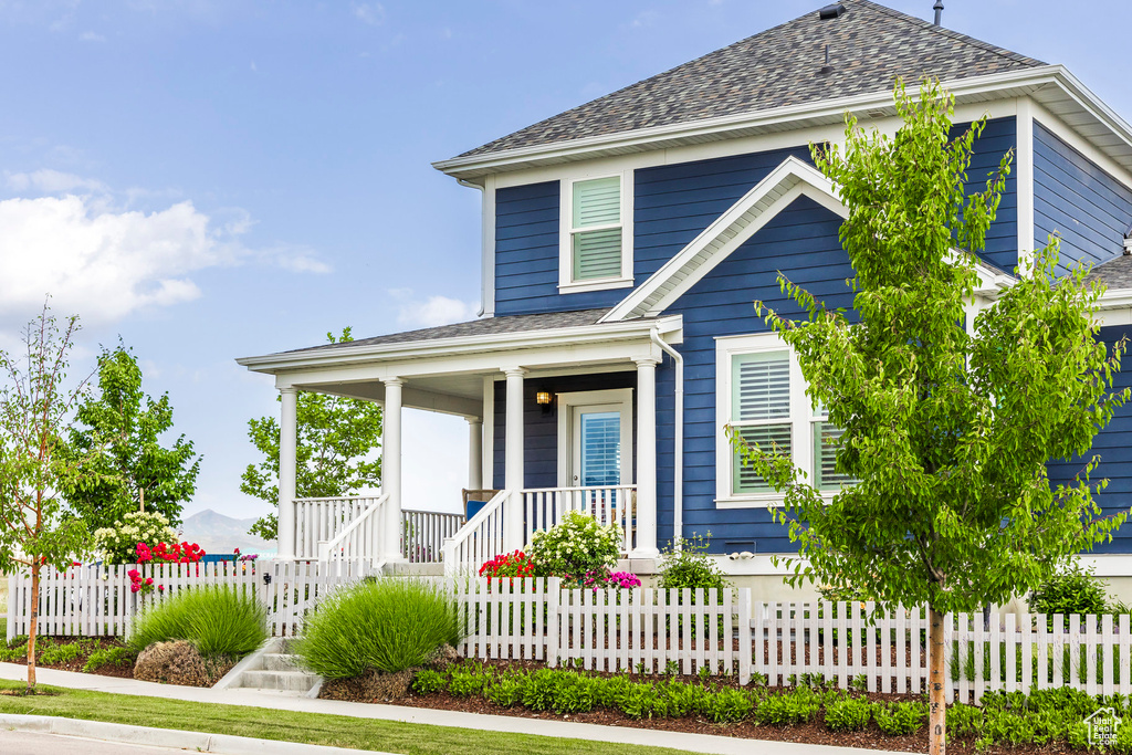 View of front of home with a porch, a shingled roof, and a fenced front yard