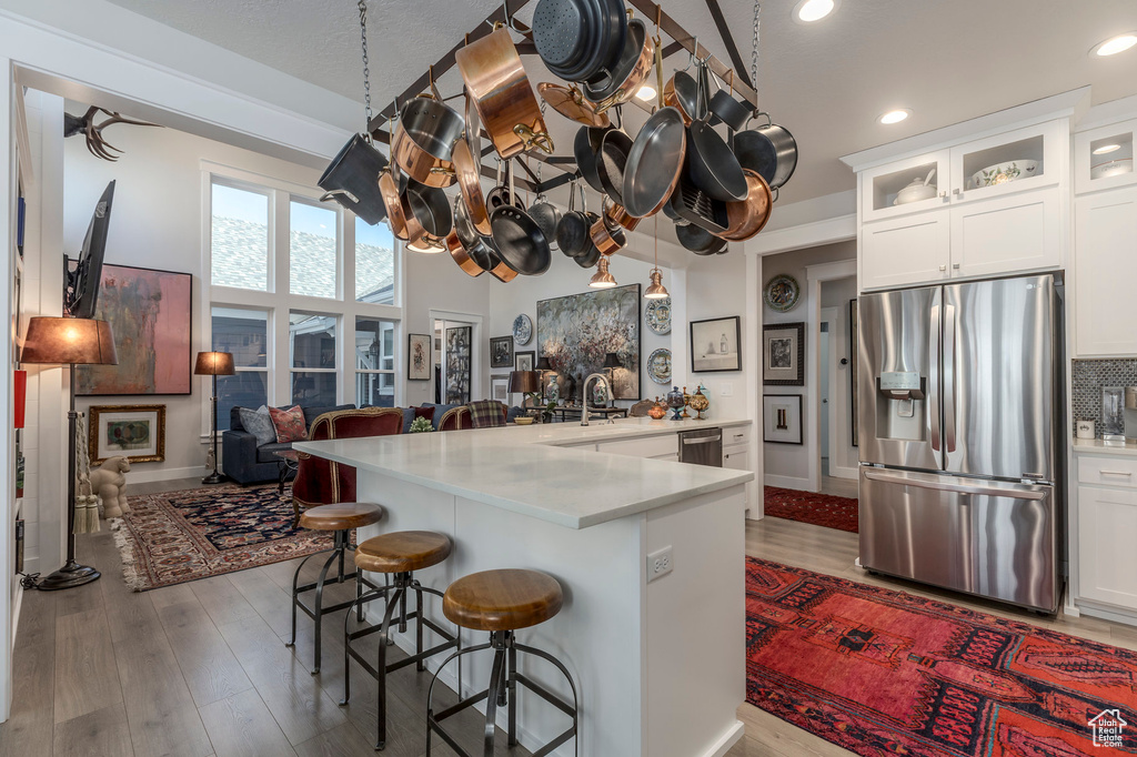 Kitchen featuring stainless steel appliances, a kitchen bar, wood finished floors, glass insert cabinets, and white cabinets