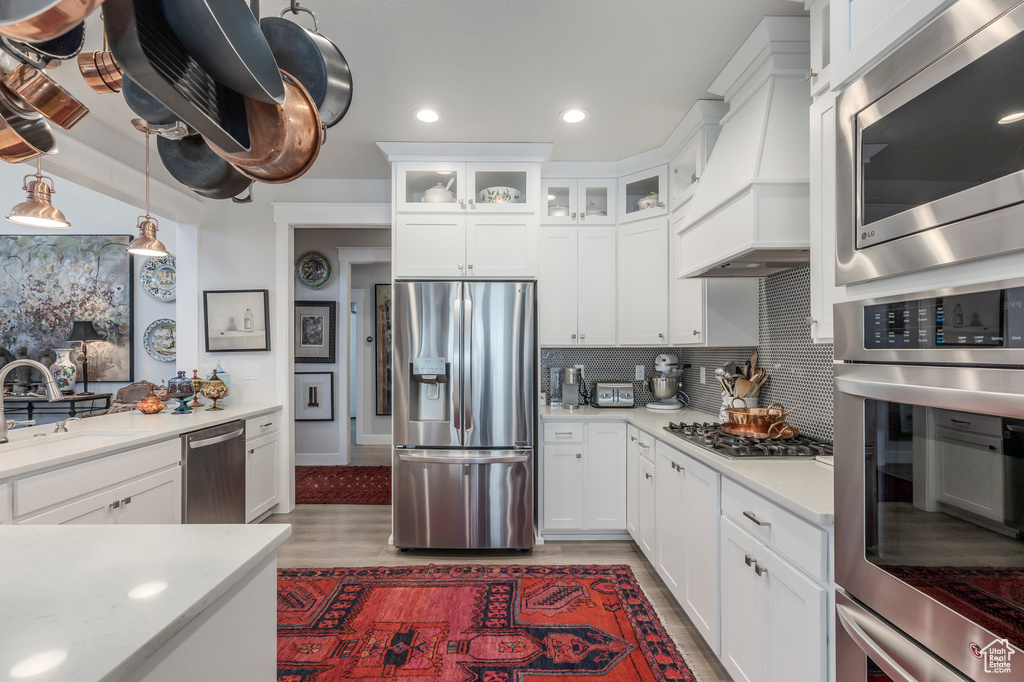 Kitchen featuring stainless steel appliances, a sink, custom range hood, light countertops, and white cabinetry