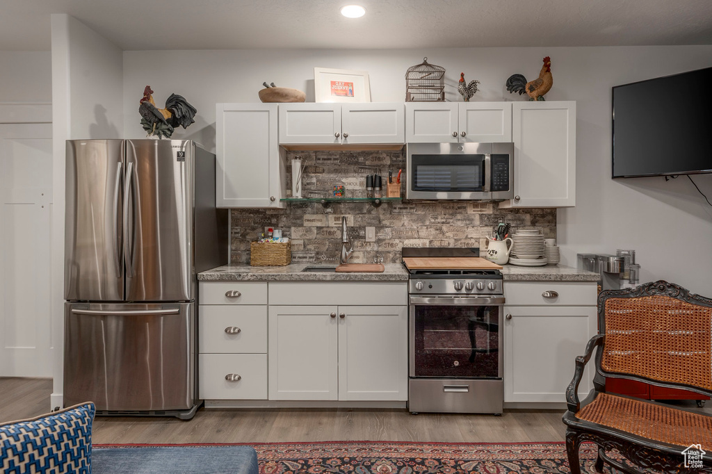 Kitchen with appliances with stainless steel finishes, a sink, light wood-type flooring, white cabinets, and recessed lighting