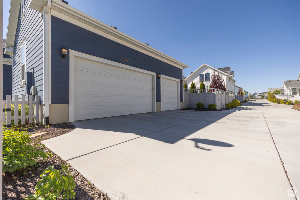 View of side of property with fence, a garage, concrete driveway, and a residential view