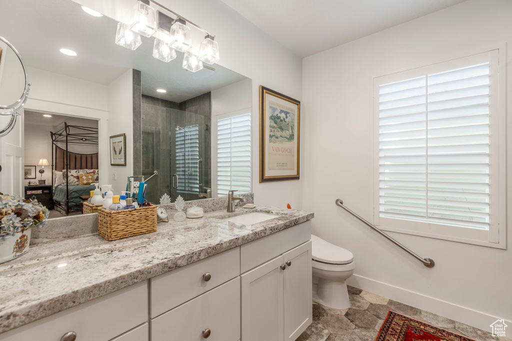 Ensuite bathroom with plenty of natural light, a shower with door, stone finish flooring, and baseboards