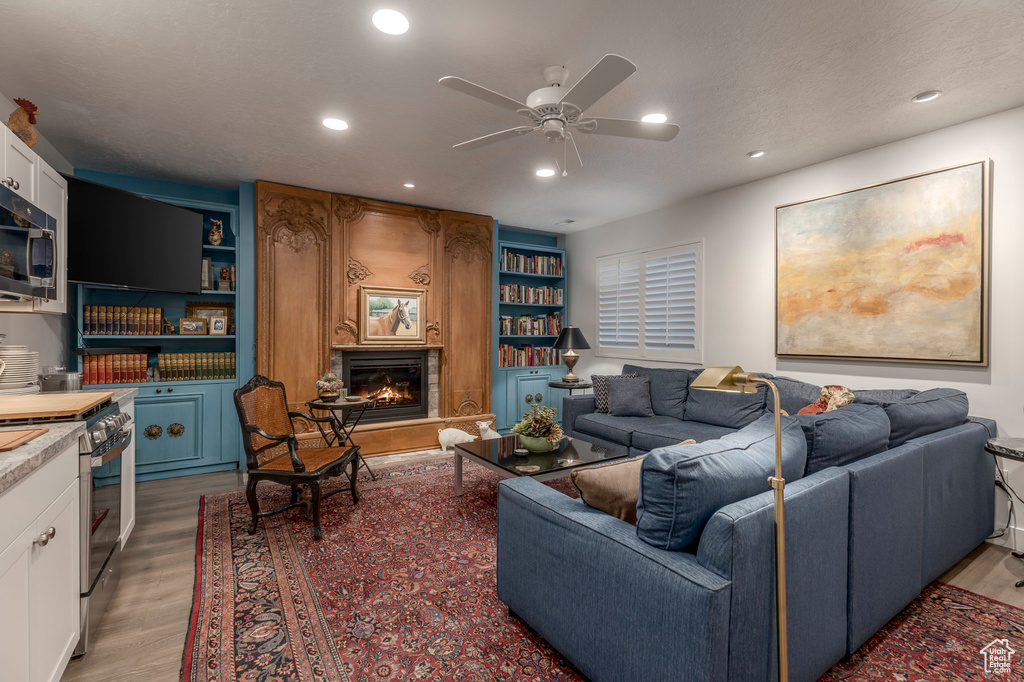 Living room featuring light wood-style flooring, ceiling fan, a fireplace, recessed lighting, and built in shelves