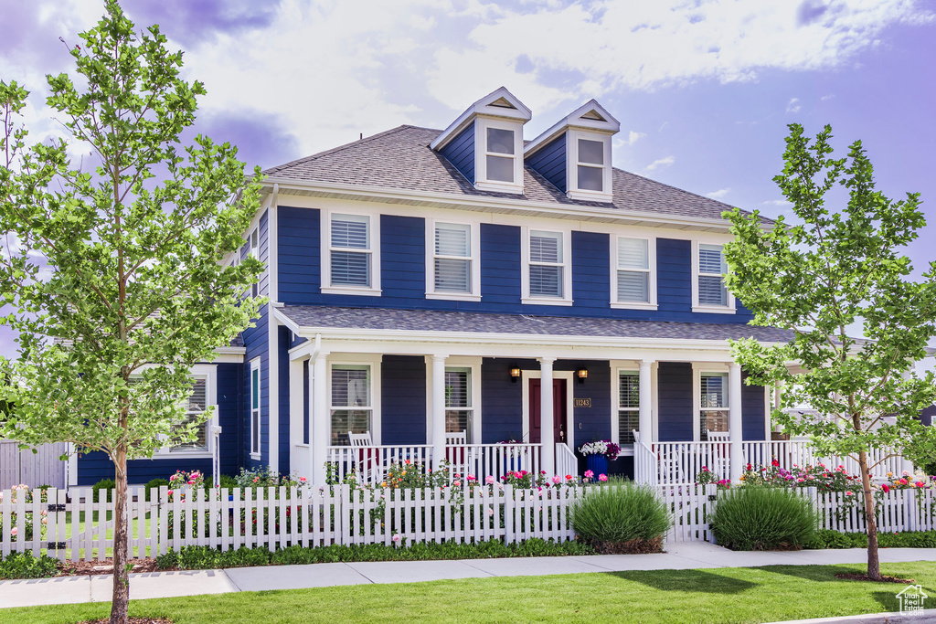 View of front of home featuring covered porch, a fenced front yard, and a shingled roof