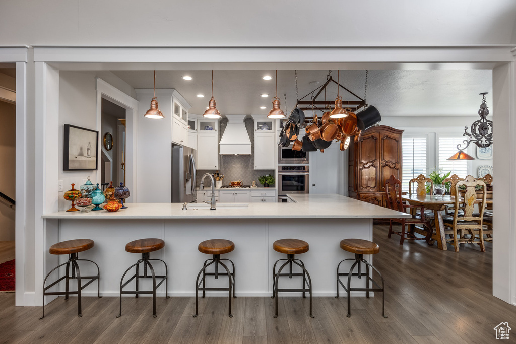 Kitchen with stainless steel appliances, a sink, white cabinets, custom range hood, and dark wood-style floors