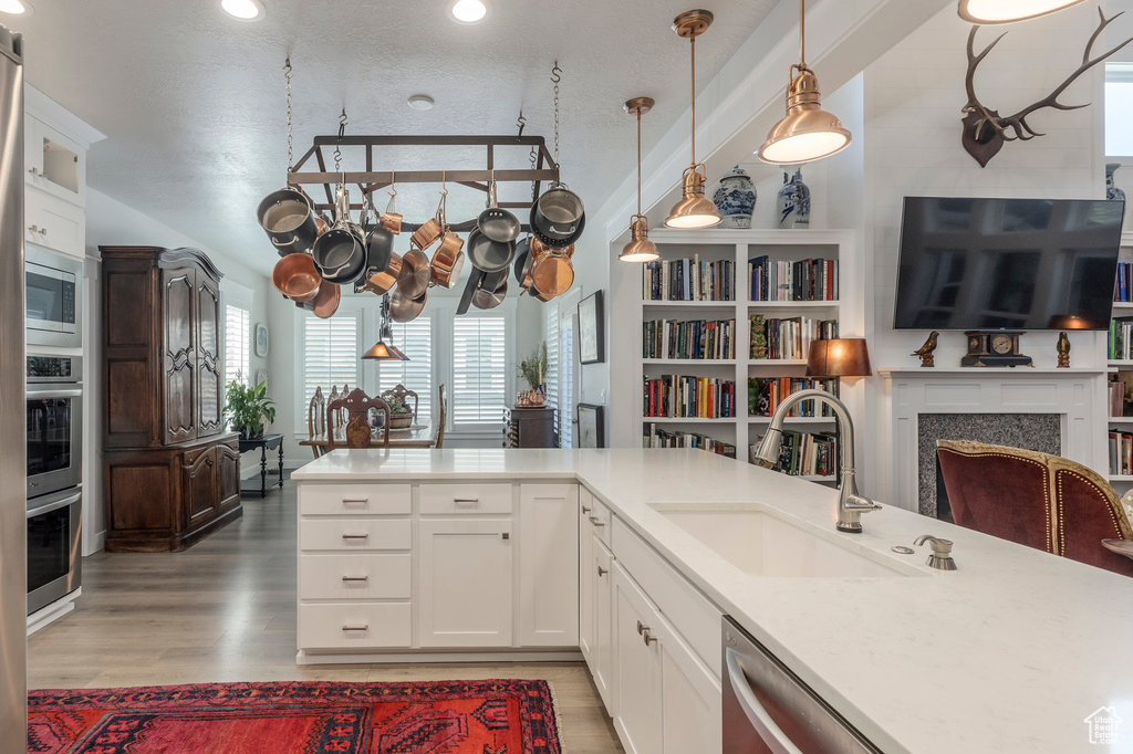 Kitchen with a sink, light wood-style flooring, hanging light fixtures, appliances with stainless steel finishes, and recessed lighting