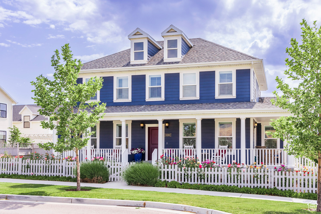 View of front of property with covered porch, a fenced front yard, and a shingled roof