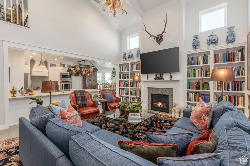 Living area with high vaulted ceiling, a glass covered fireplace, wood finished floors, and a chandelier