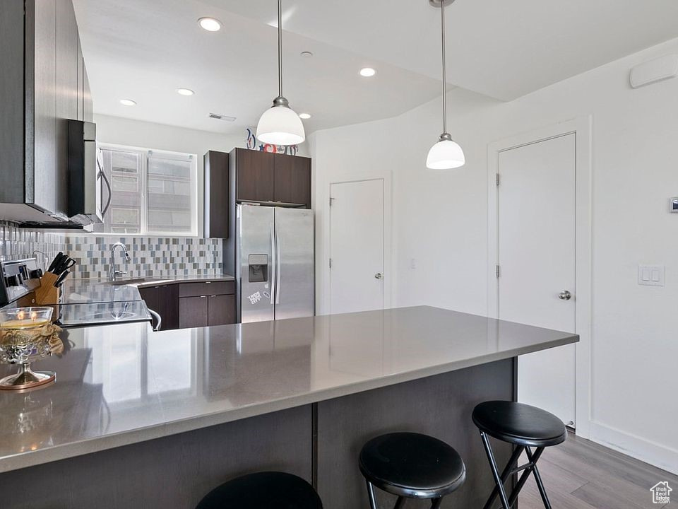 Kitchen with appliances with stainless steel finishes, a peninsula, a breakfast bar area, light wood finished floors, and recessed lighting