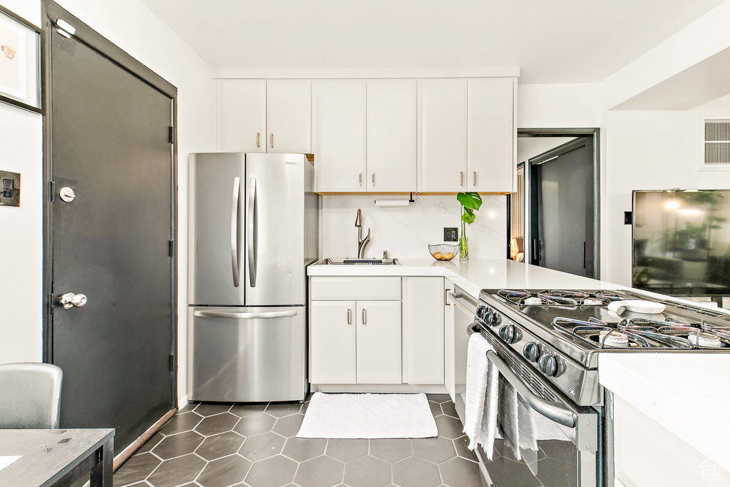 Kitchen featuring freestanding refrigerator, gas stove, a sink, light countertops, and white cabinetry