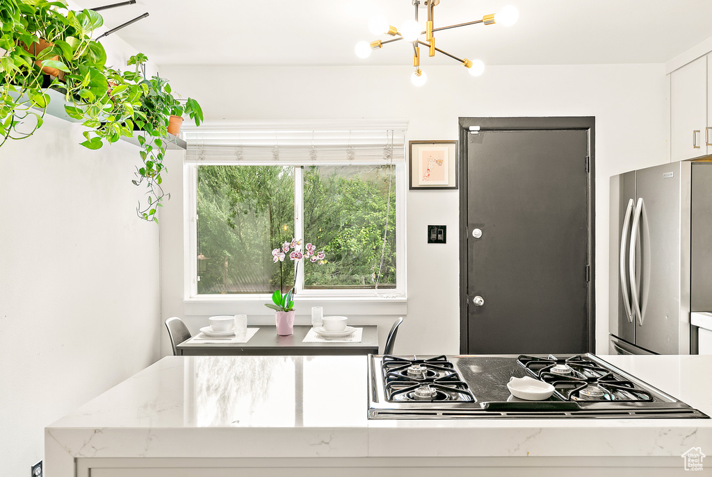 Kitchen featuring freestanding refrigerator, gas stovetop, a chandelier, white cabinetry, and light stone counters