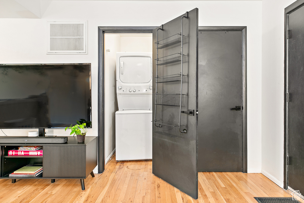 Washroom with stacked washer and clothes dryer, wood-type flooring, and baseboards