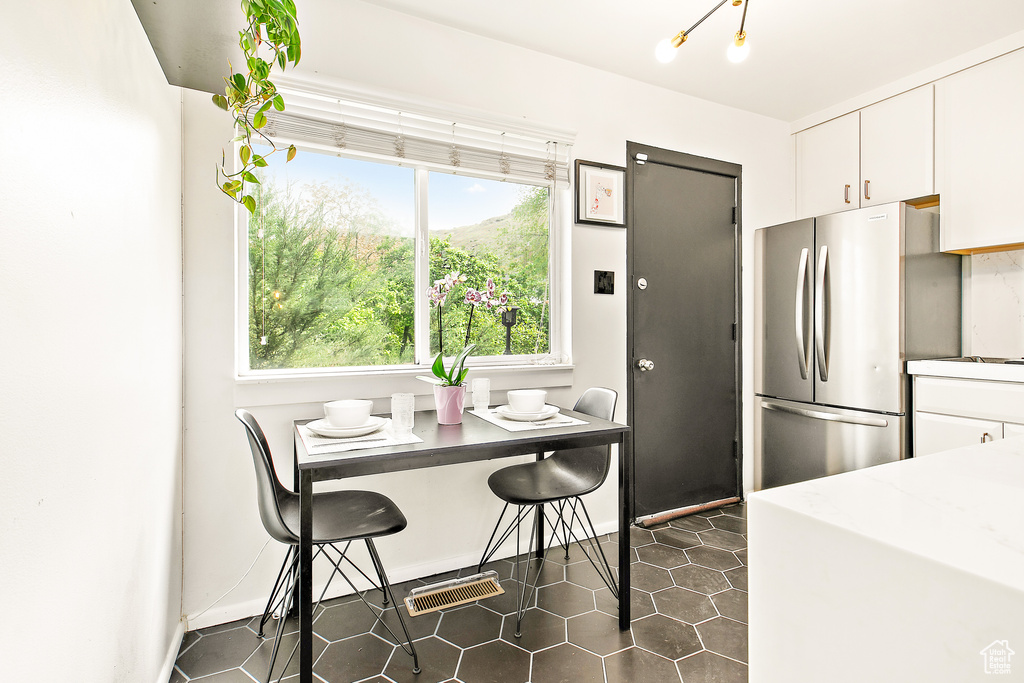 Kitchen with freestanding refrigerator, white cabinets, dark tile patterned floors, and baseboards