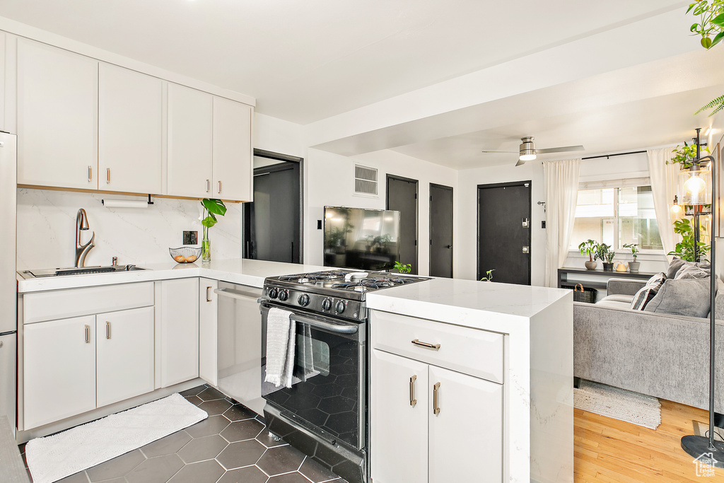Kitchen featuring appliances with stainless steel finishes, open floor plan, a sink, a peninsula, and light countertops