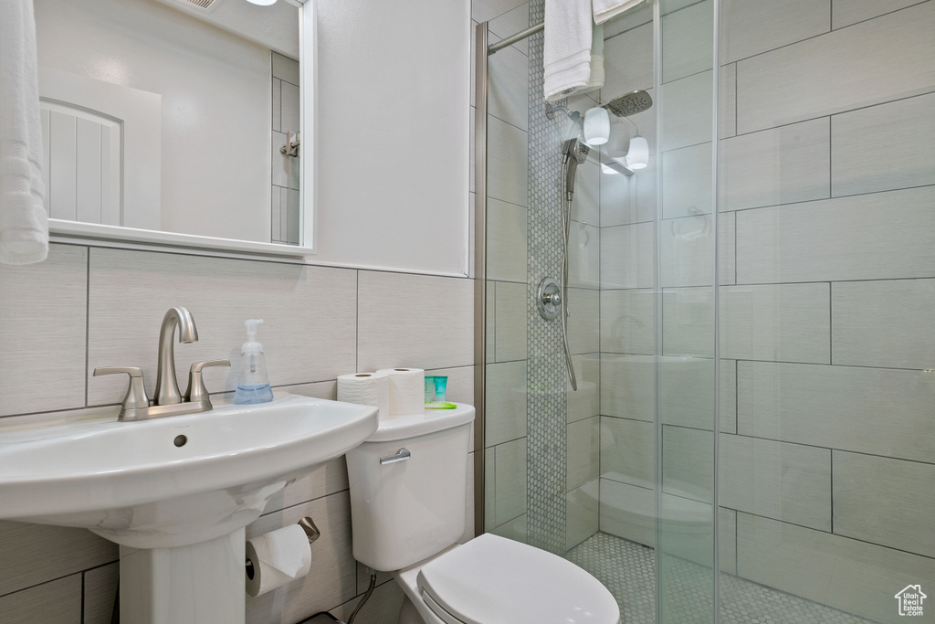 Bathroom featuring toilet, tile walls, a shower stall, a sink, and backsplash