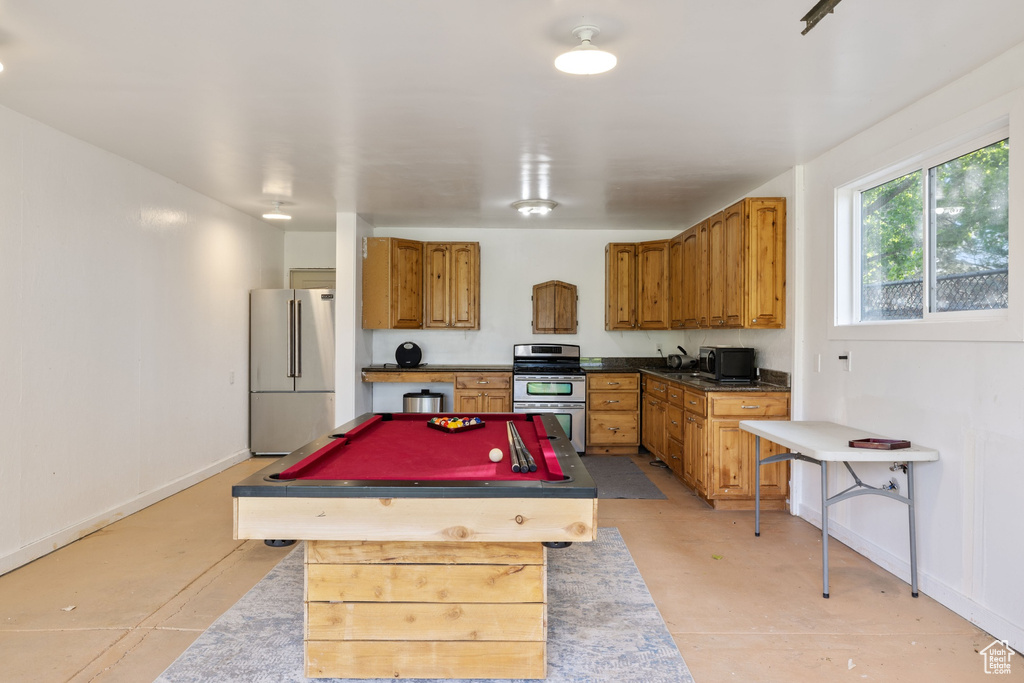 Kitchen featuring stainless steel appliances, a center island, billiards, brown cabinets, and baseboards
