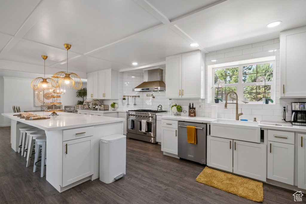 Kitchen featuring wall chimney range hood, tasteful backsplash, a sink, coffered ceiling, and appliances with stainless steel finishes