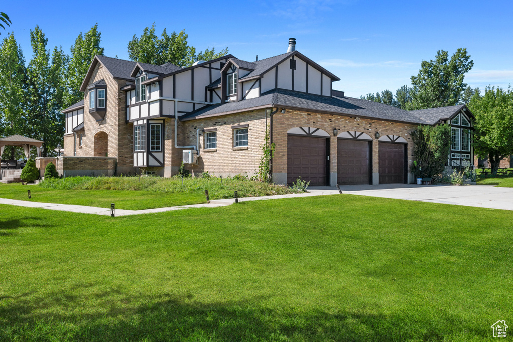 Tudor home featuring an attached garage, driveway, brick siding, and a front yard